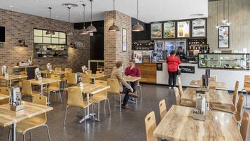 A modern cafe interior with wooden tables and chairs, a brick accent wall, and a counter with a menu.