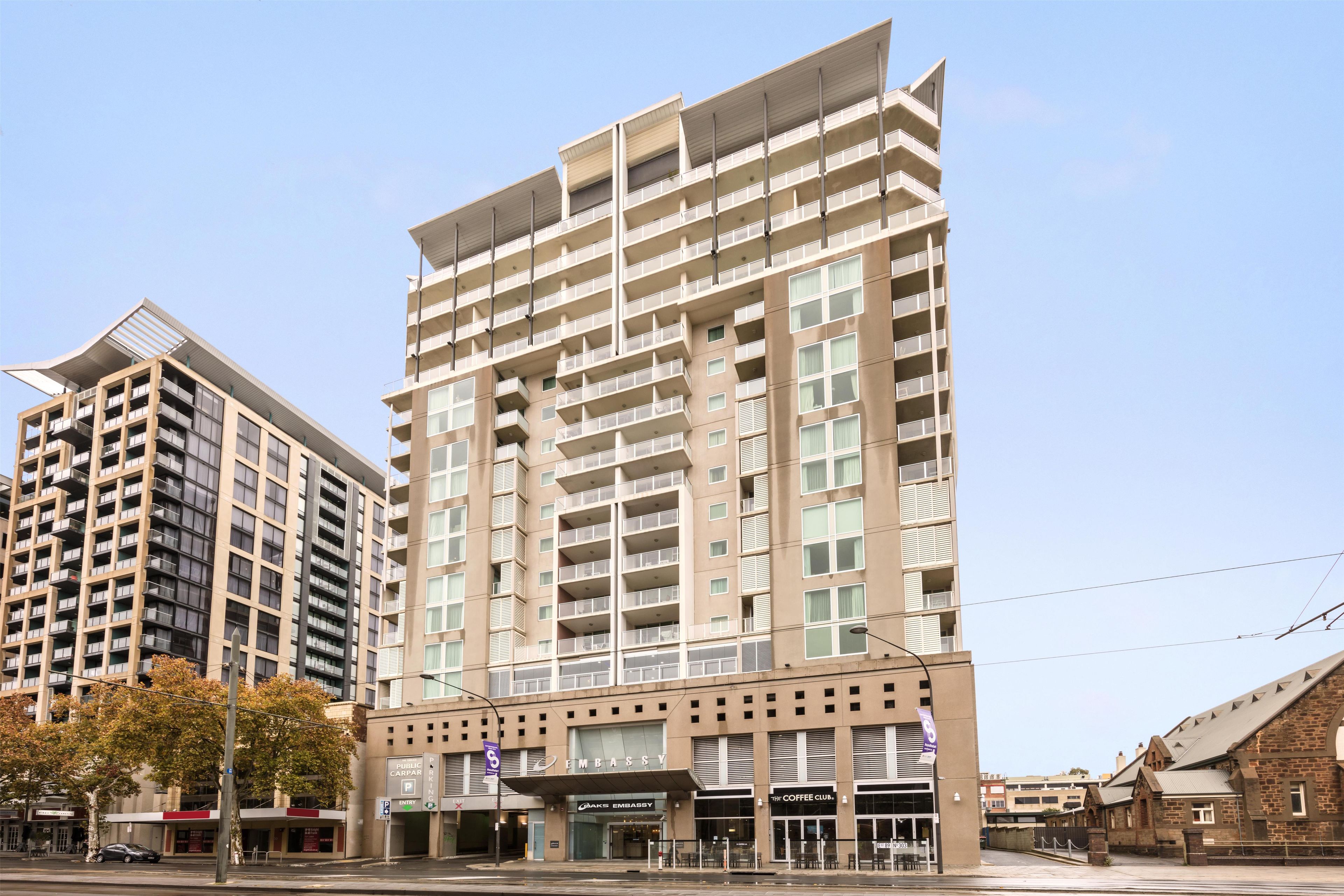 A multi-story building with a flat facade, multiple balconies, and a ground-level entrance with signage for a coffee shop and a public car park.