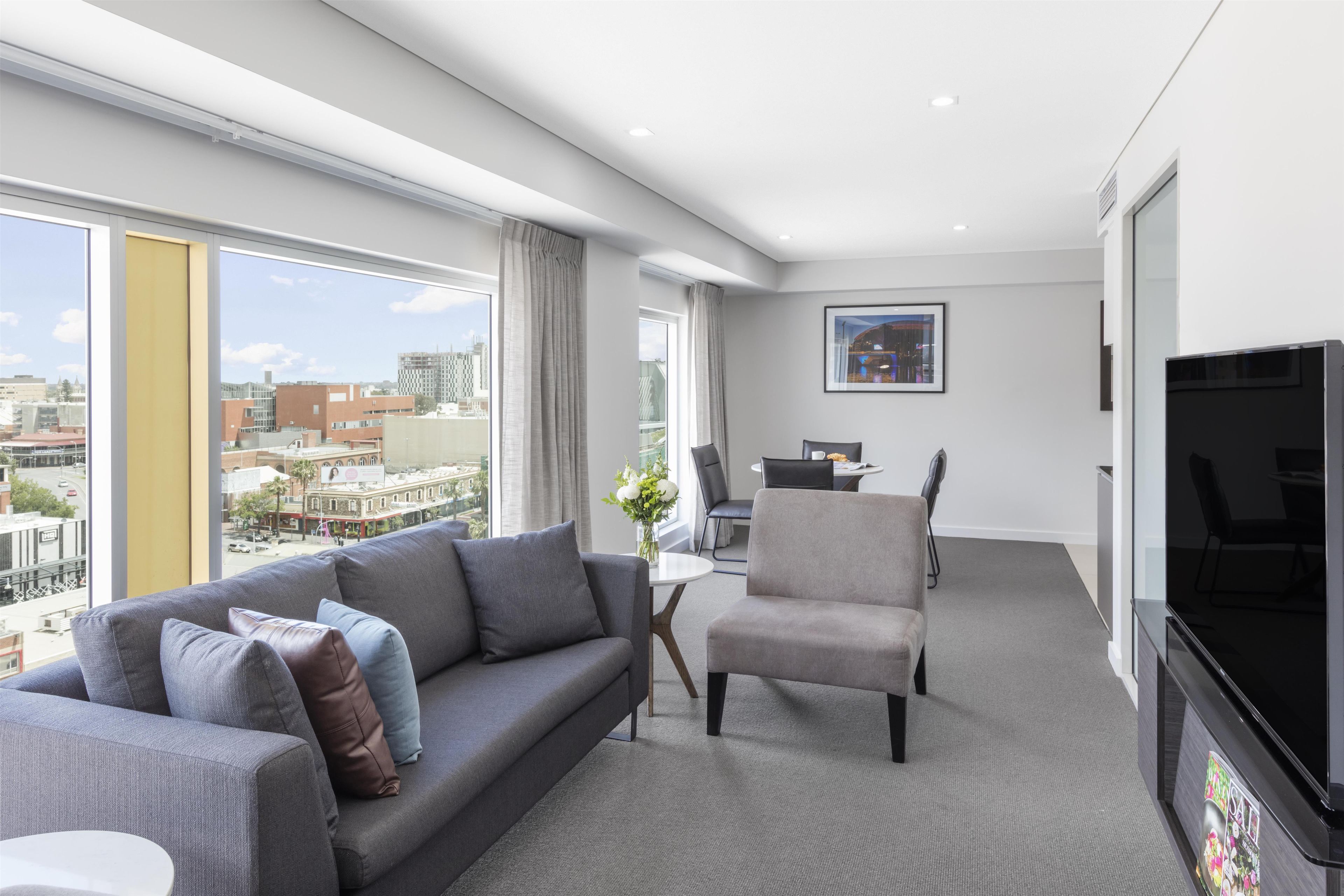 Ein modernes Hotelzimmer mit Sofa, Sessel, Esstisch und Fernseher.