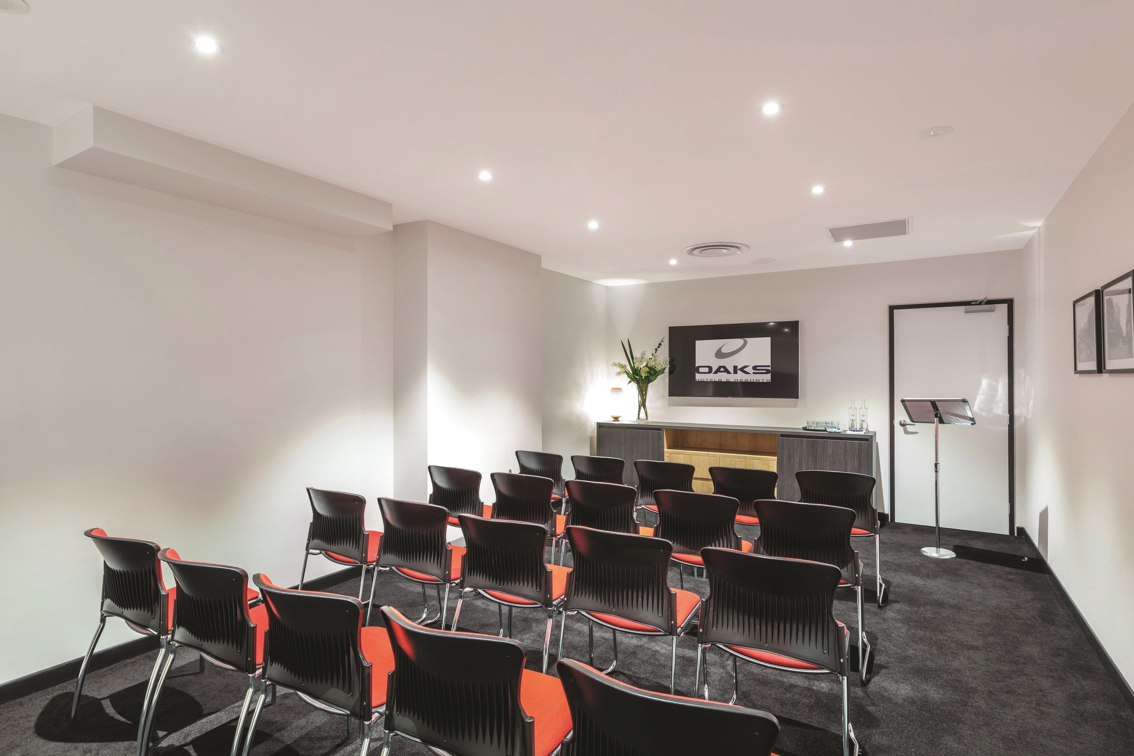A conference room with rows of chairs, a reception desk, and a flat-screen TV on the wall.
