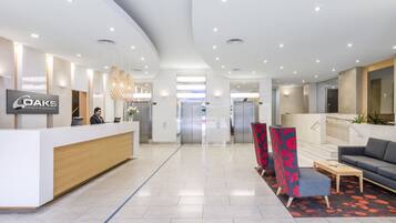 A modern hotel reception area with a reception desk, seating area, and elevators.