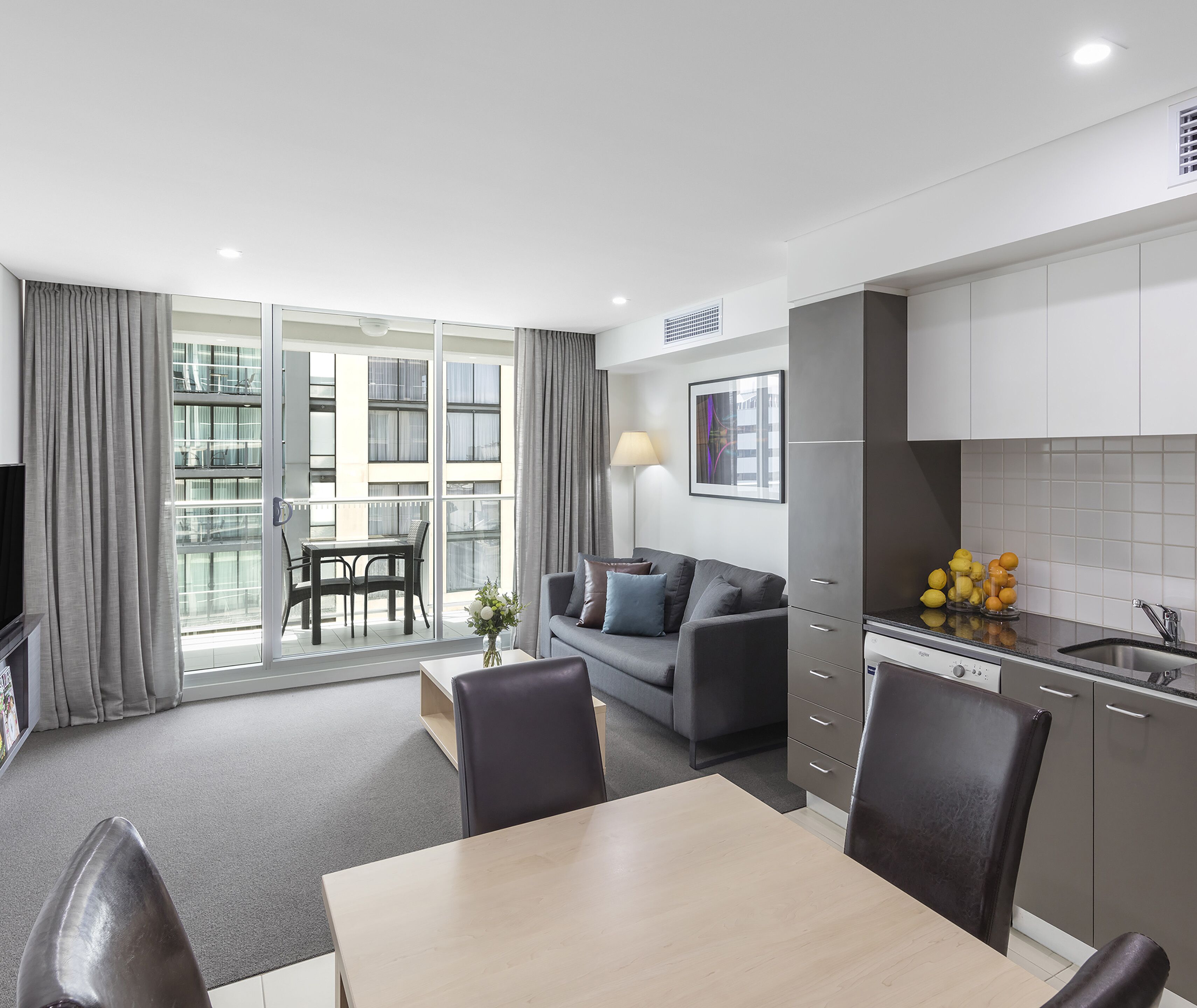 A modern apartment with a dining area, sofa, kitchen, and large windows.