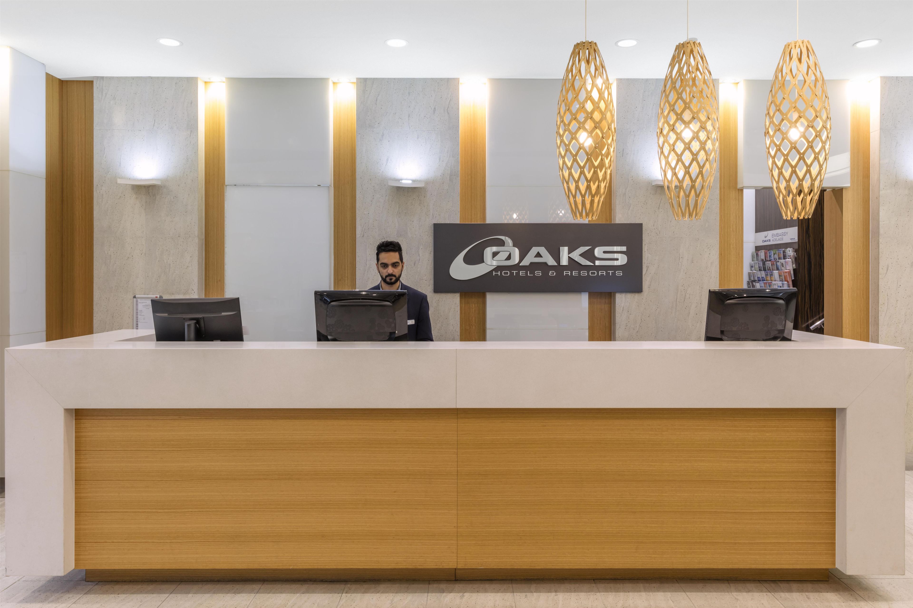 Ein Empfangsschalter mit einem Schild für 'OAKS HOTELS & RESORTS' und drei Computermonitoren.