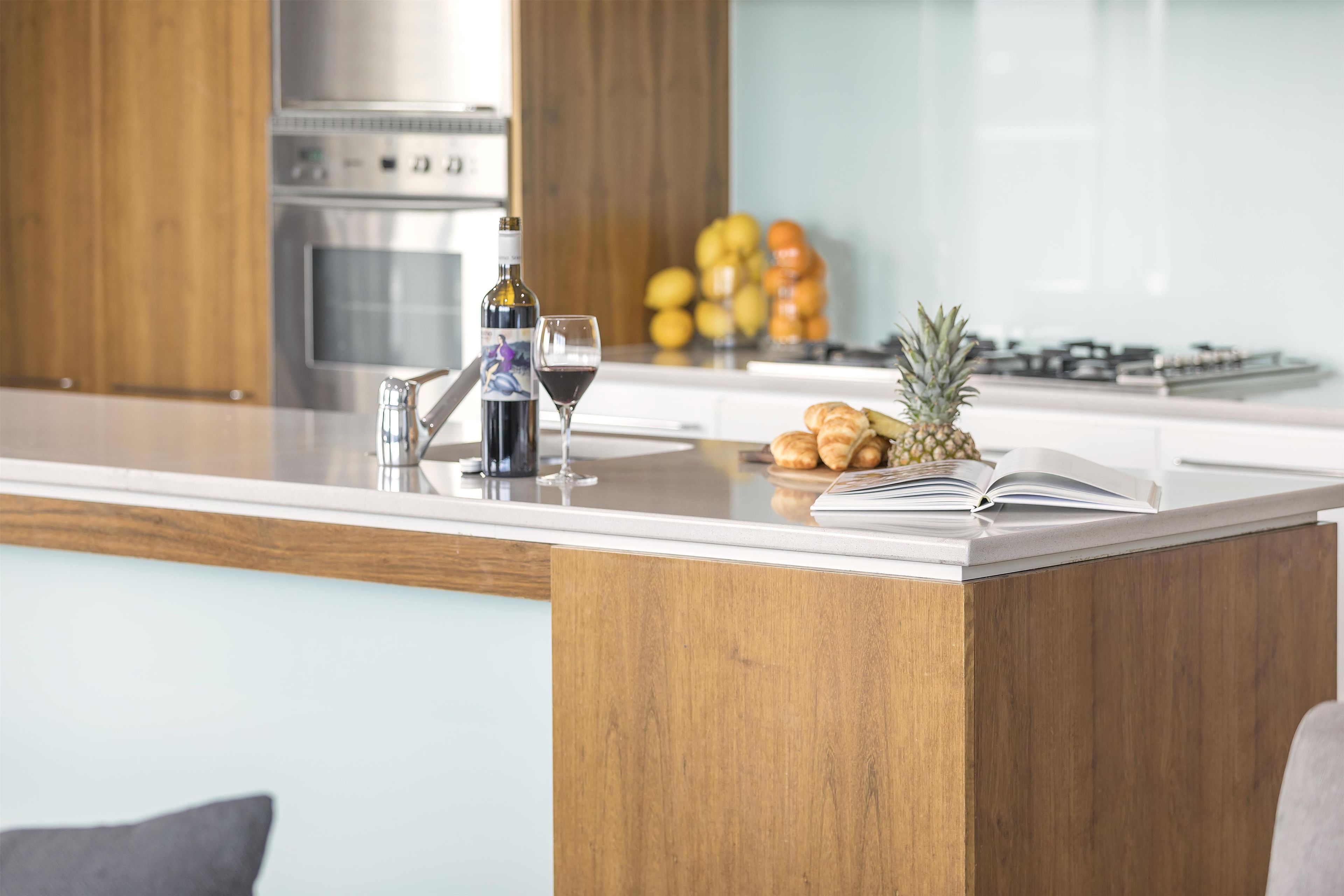 A modern kitchen with a wooden countertop, a wine bottle, a glass of red wine, a pineapple, and a book.