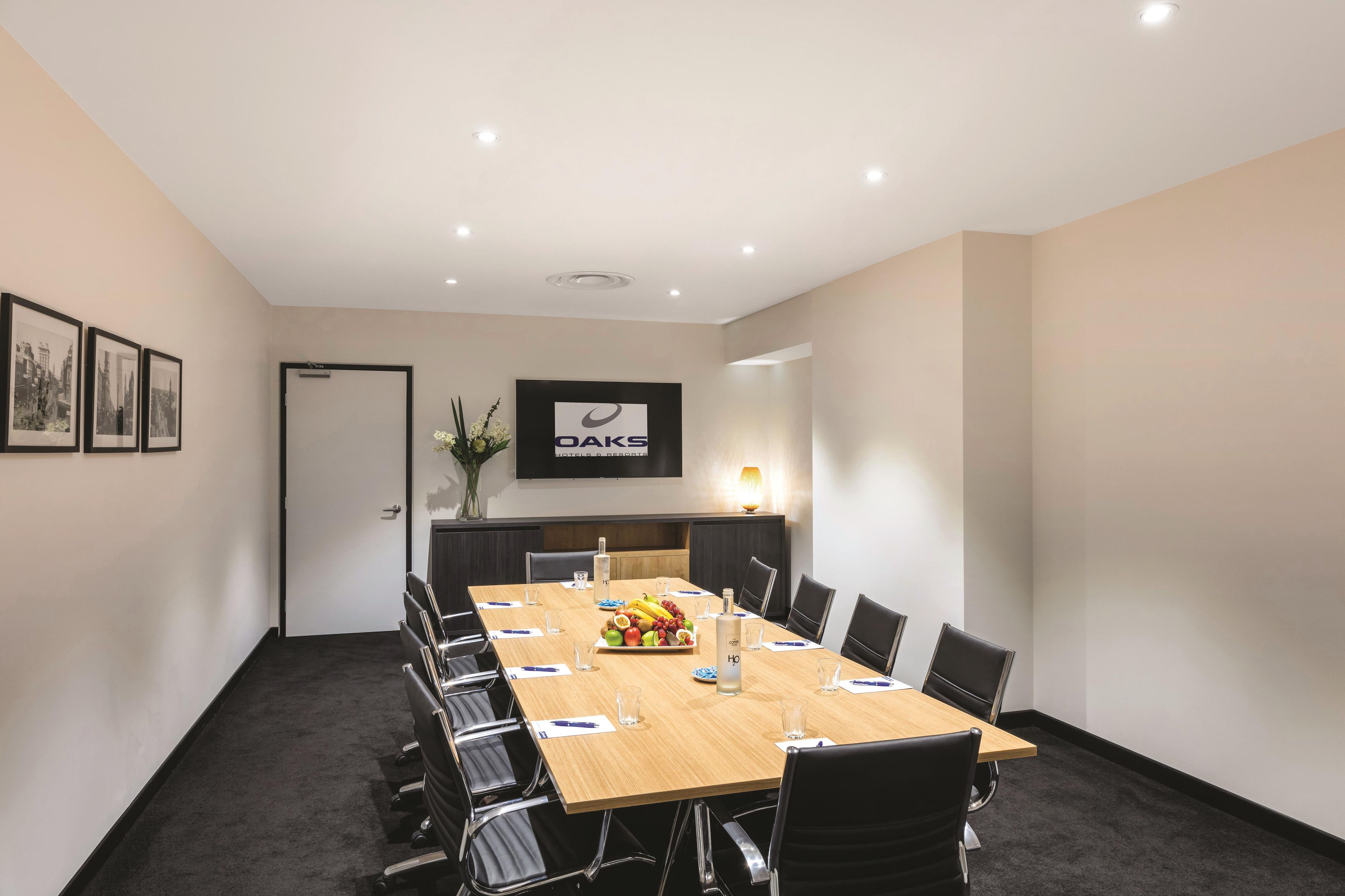 A conference room with a long table, chairs, a television screen, and framed pictures on the wall.