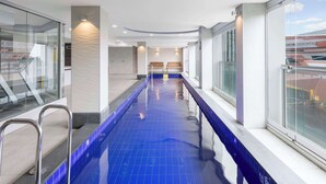 Una piscina con paredes de vidrio transparente en un lado y un diseño interior moderno con suelo de baldosas azules.
