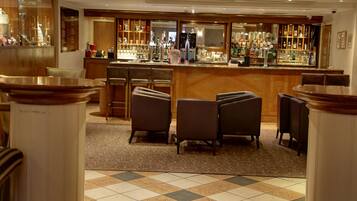 A bar area with a checkered floor, bar stools, and a variety of bottles and glasses on shelves.