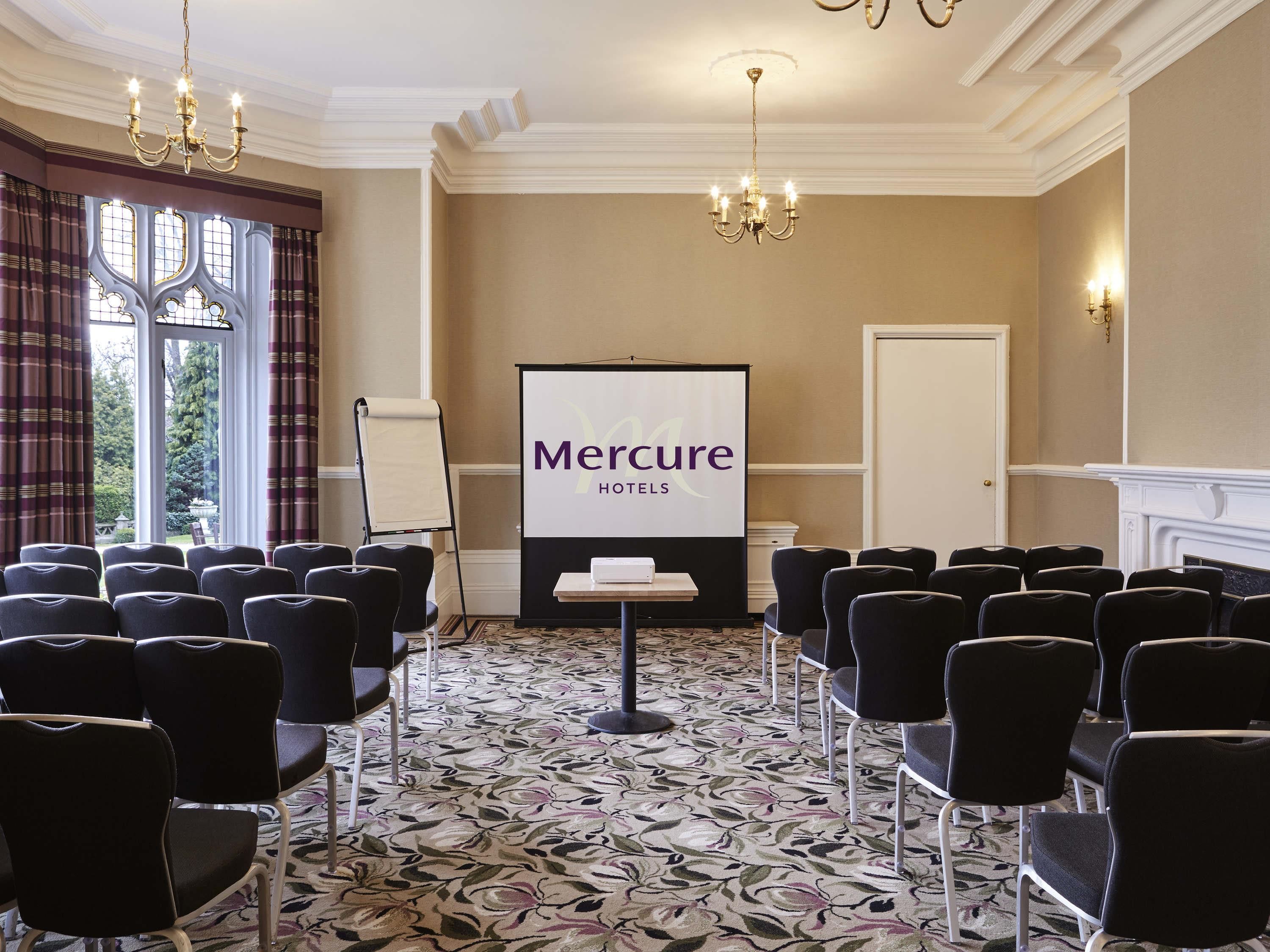 A conference room with rows of chairs, a projection screen, and a fireplace.