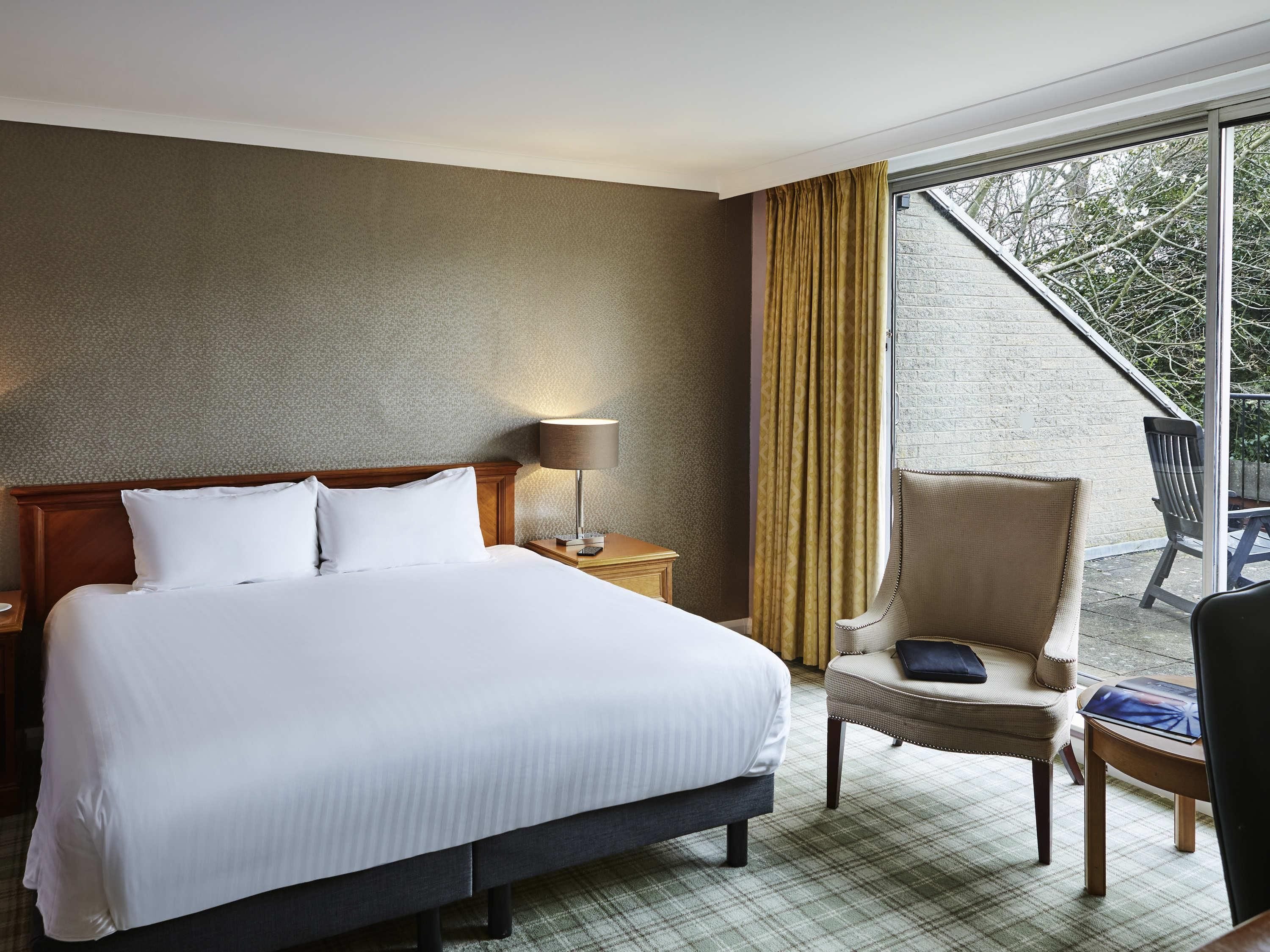 Une chambre d’hôtel avec un grand lit, une table de chevet avec une lampe, une chaise et une vue sur l’extérieur.