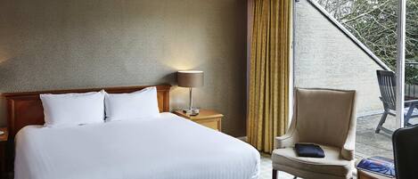 A hotel room with a large bed, a bedside table with a lamp, a chair, and a view of the outdoors.