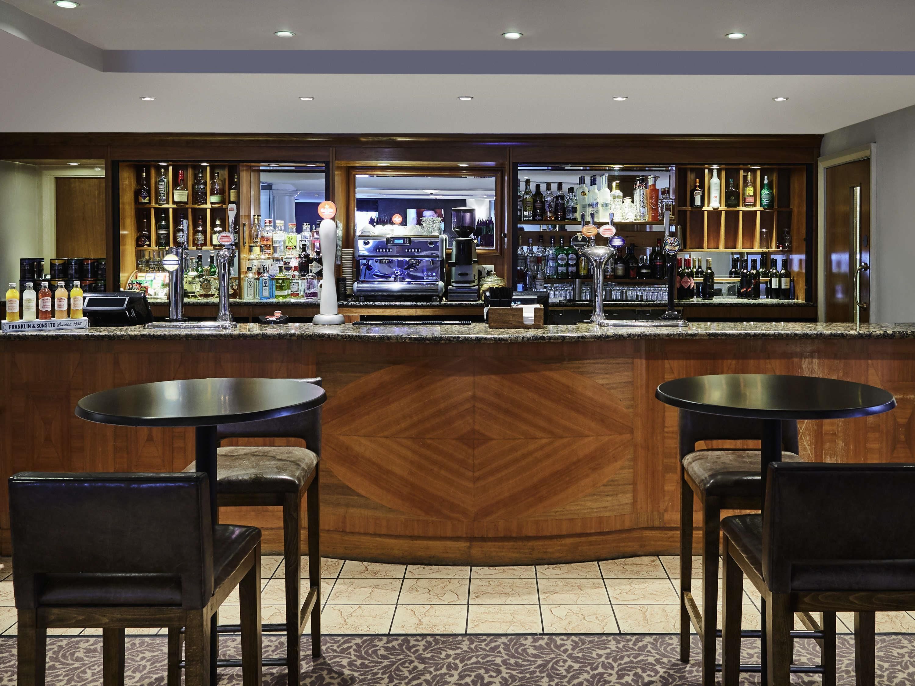 A bar area with two round tables and chairs, a counter with a variety of bottles, and a coffee machine.