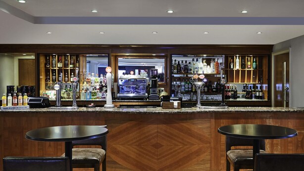 A bar area with two round tables and chairs, a counter with a variety of bottles, and a coffee machine. - Mercure Sheffield Kenwood Hall & Spa (Sheffield)