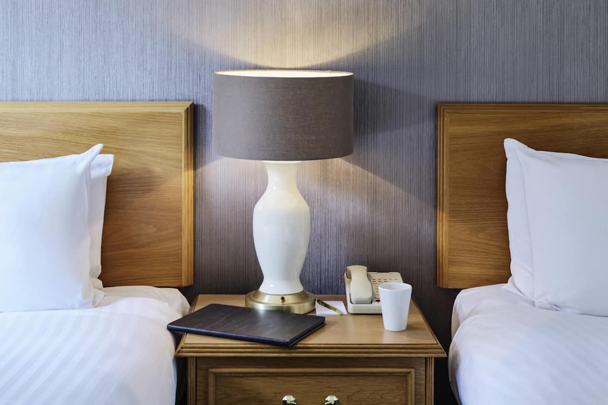 Ein Hotelzimmer mit einem Bett, einem Nachttisch, einer Lampe, einem Telefon und einer Tasse.