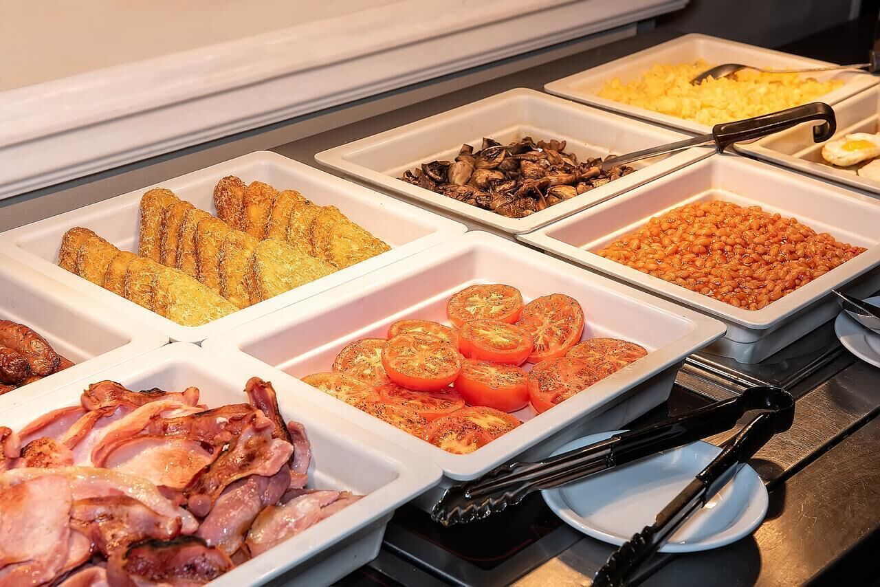 Un bufé con diversas opciones de comida, incluyendo tocino, tomates, champiñones y otros platos.