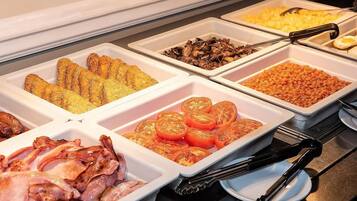 Un bufé con diversas opciones de comida, incluyendo tocino, tomates, champiñones y otros platos.