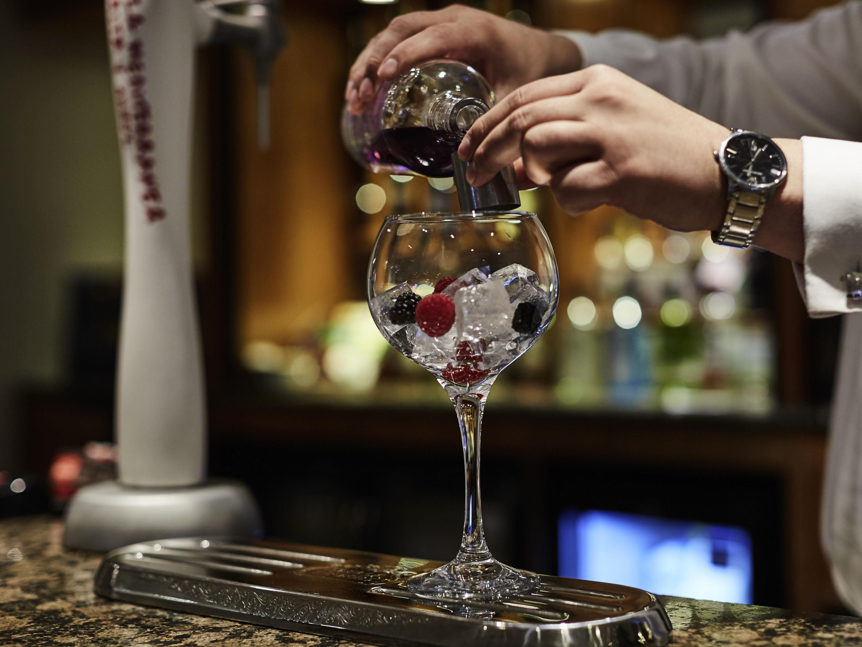 A bartender pouring a drink into a martini glass with ice and berries.