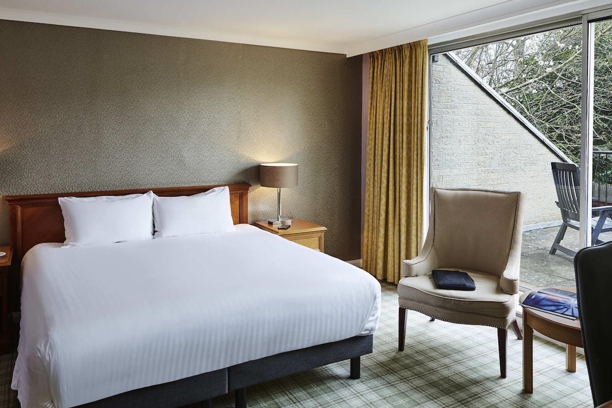Ein Hotelzimmer mit Bett, Stuhl, Lampe und Blick ins Freie.
