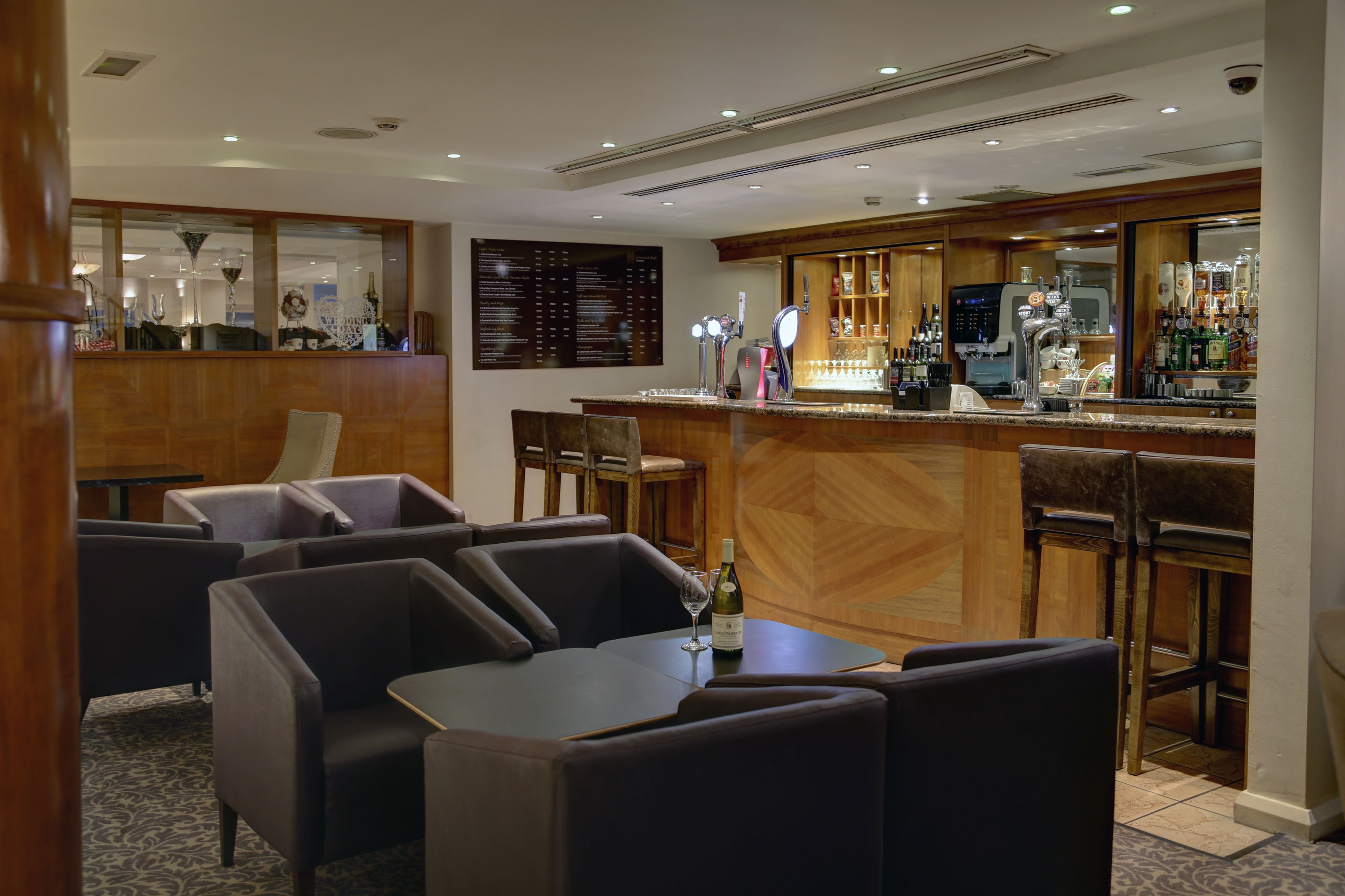 A bar area with seating, a menu board, and a wine bottle on a table.