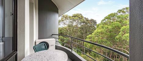 A balcony with a round table and chairs, a view of trees, and a railing.