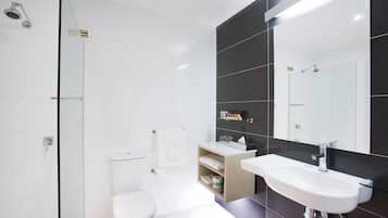 Une salle de bain moderne avec une douche à parois de verre, des toilettes blanches, un meuble-lavabo avec un miroir et un évier.