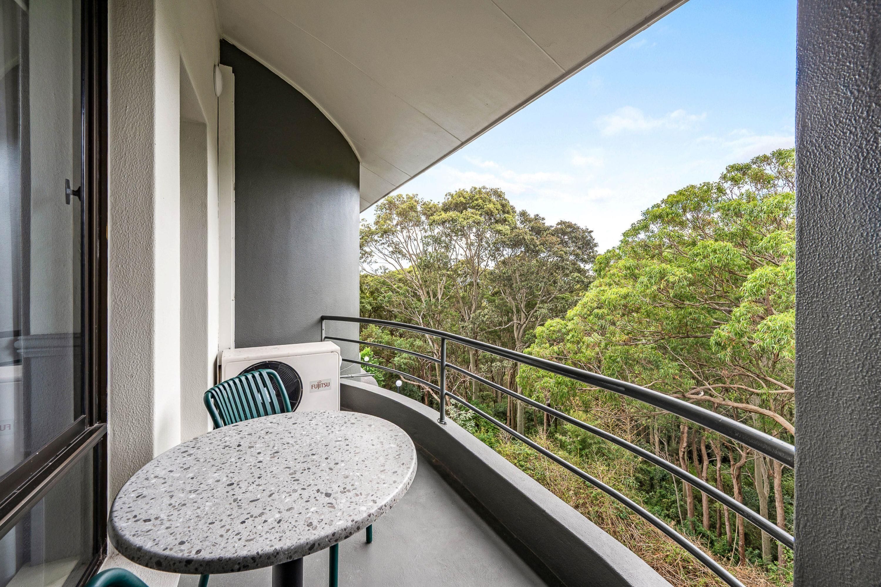 Un balcon avec une table ronde et des chaises, une vue sur les arbres et une balustrade.