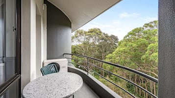 A balcony with a round table and chairs, a view of trees, and a railing.