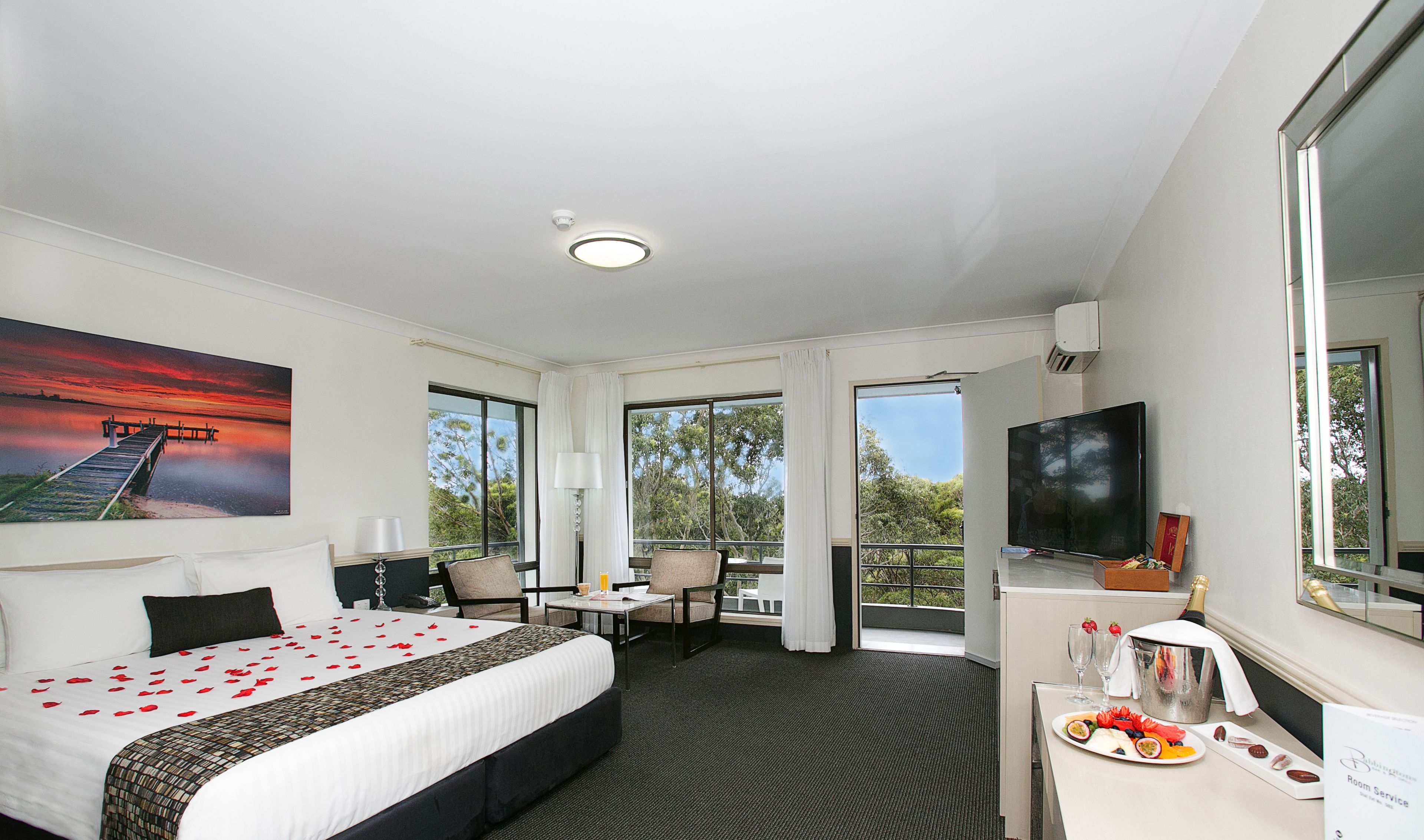 A hotel room with a bed, a desk, a TV, and a balcony with a view.