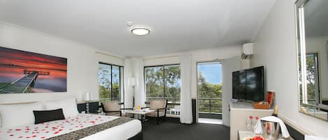 A hotel room with a bed, a desk, a TV, and a balcony with a view.