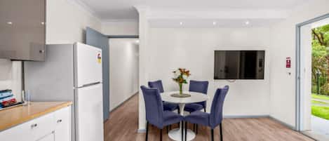 Una cocina moderna con gabinetes blancos, un refrigerador integrado y un comedor con una mesa redonda y sillas azules.