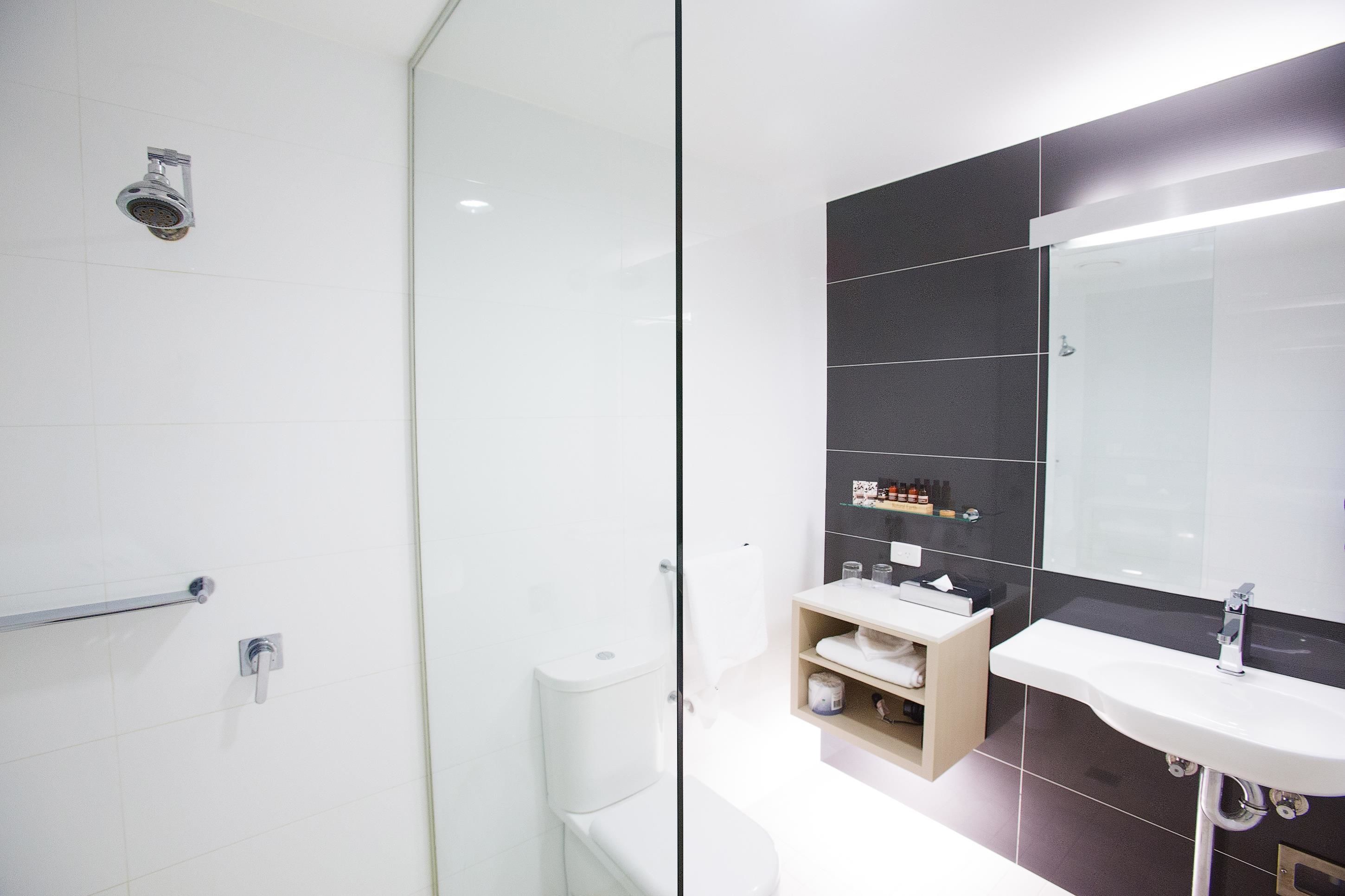 Un baño moderno con mampara de cristal, inodoro blanco y tocador con espejo y estantes.