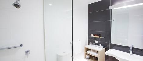 Un baño moderno con mampara de cristal, inodoro blanco y tocador con espejo y estantes.