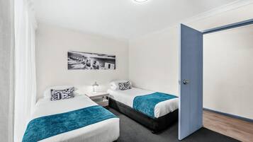 Habitación de hotel con dos camas, una mesita de noche, una lámpara, un cuadro en la pared y una puerta.