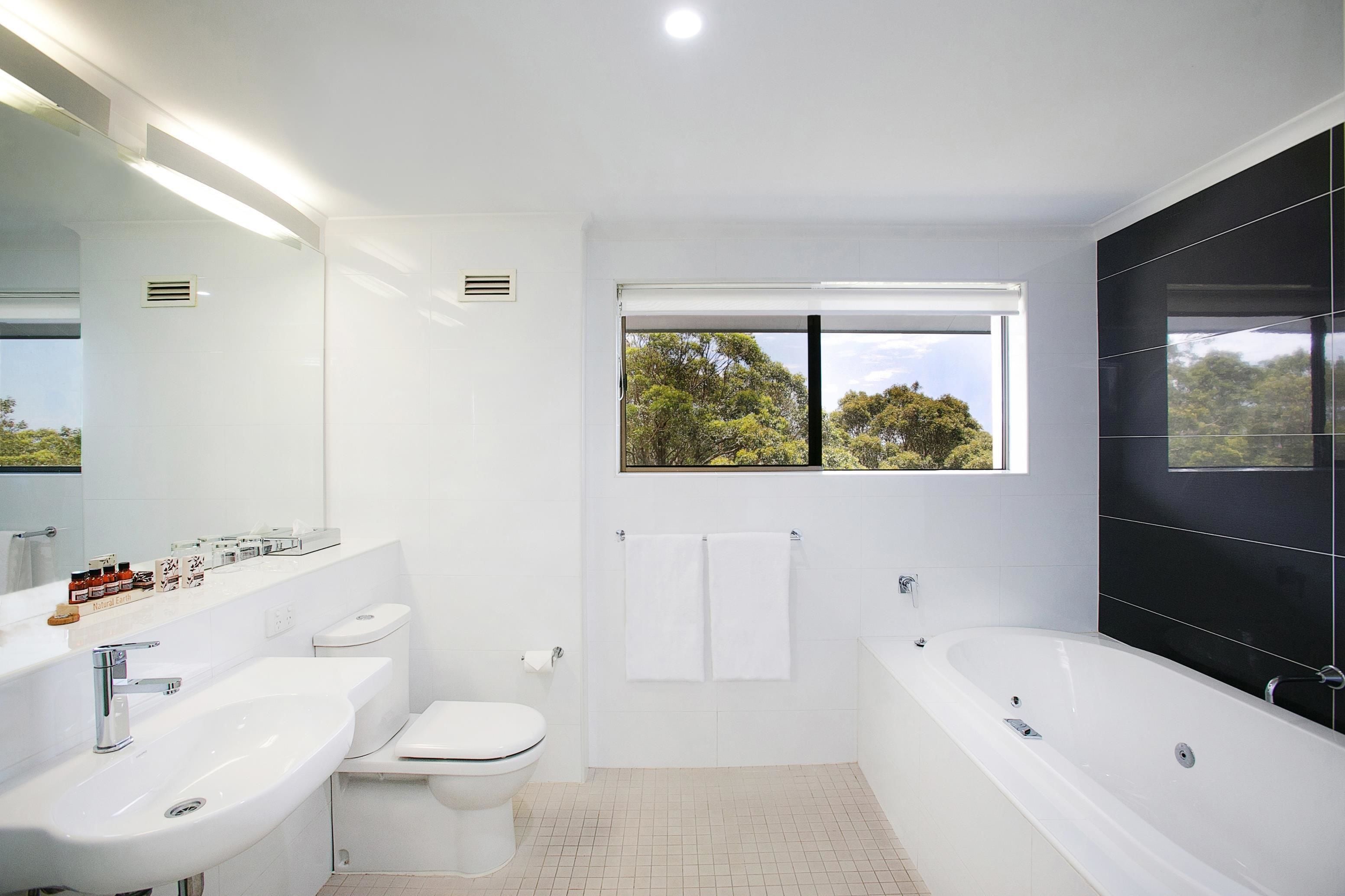 A modern bathroom with a toilet, sink, and bathtub. There is a window providing a view of trees outside.