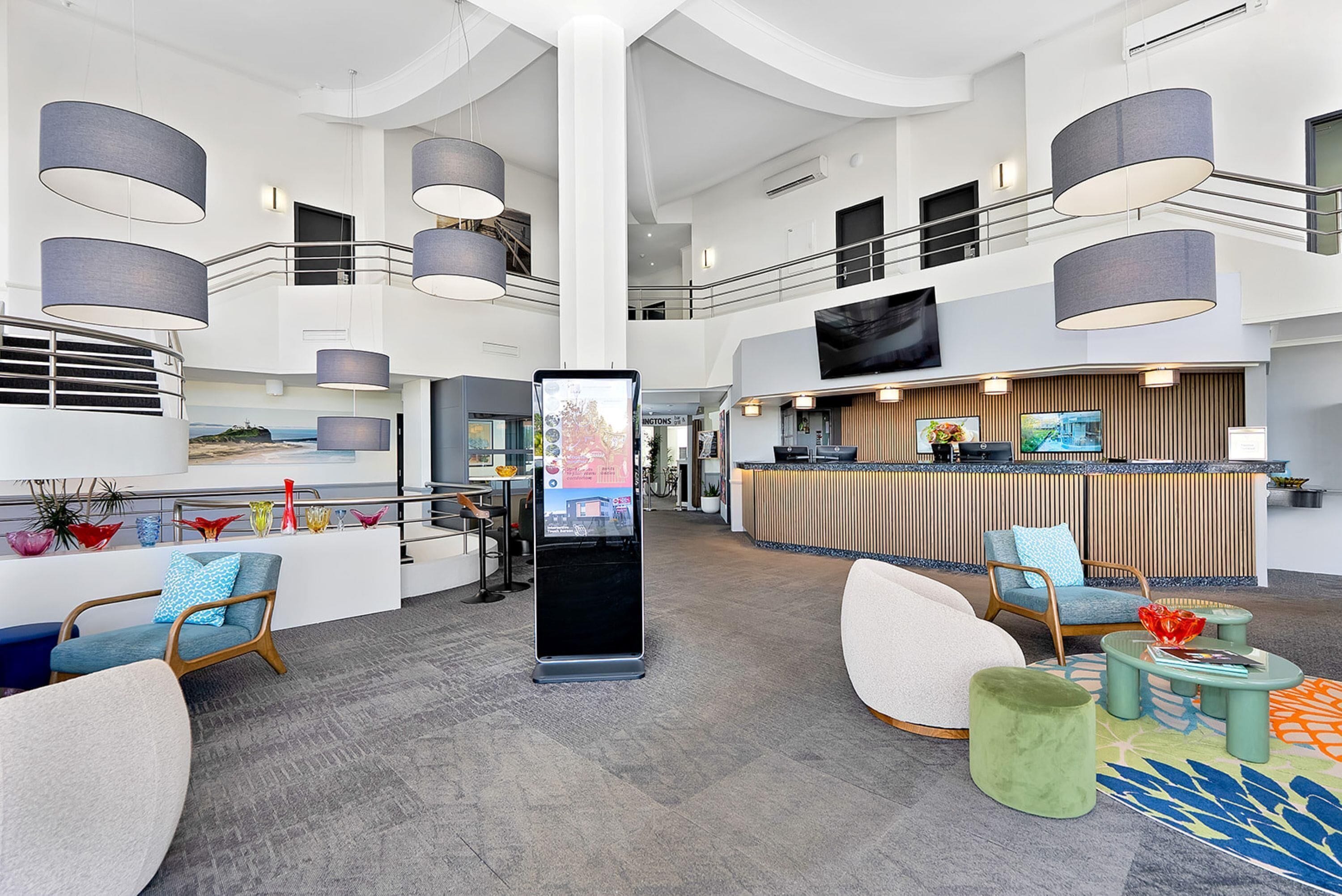 A spacious lobby with a reception desk, seating areas, and a large digital display.
