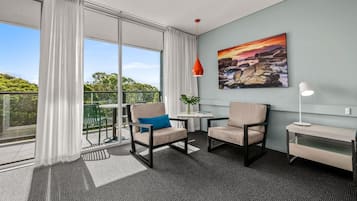 A modern room with a balcony, two chairs, a small table, a lamp, and a painting on the wall.