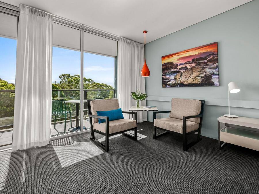 A modern room with a balcony, two chairs, a small table, a lamp, and a painting on the wall.