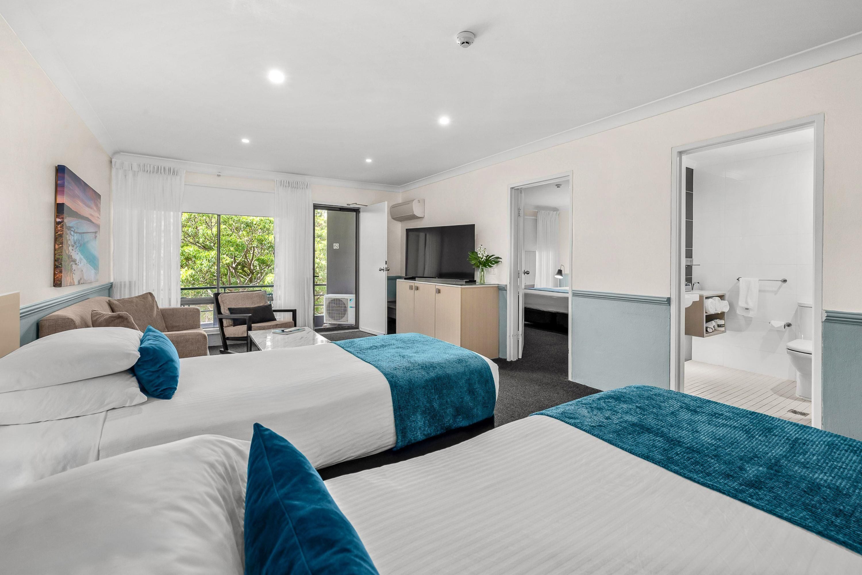 A hotel room with two beds, a desk, a chair, a TV, and a bathroom.