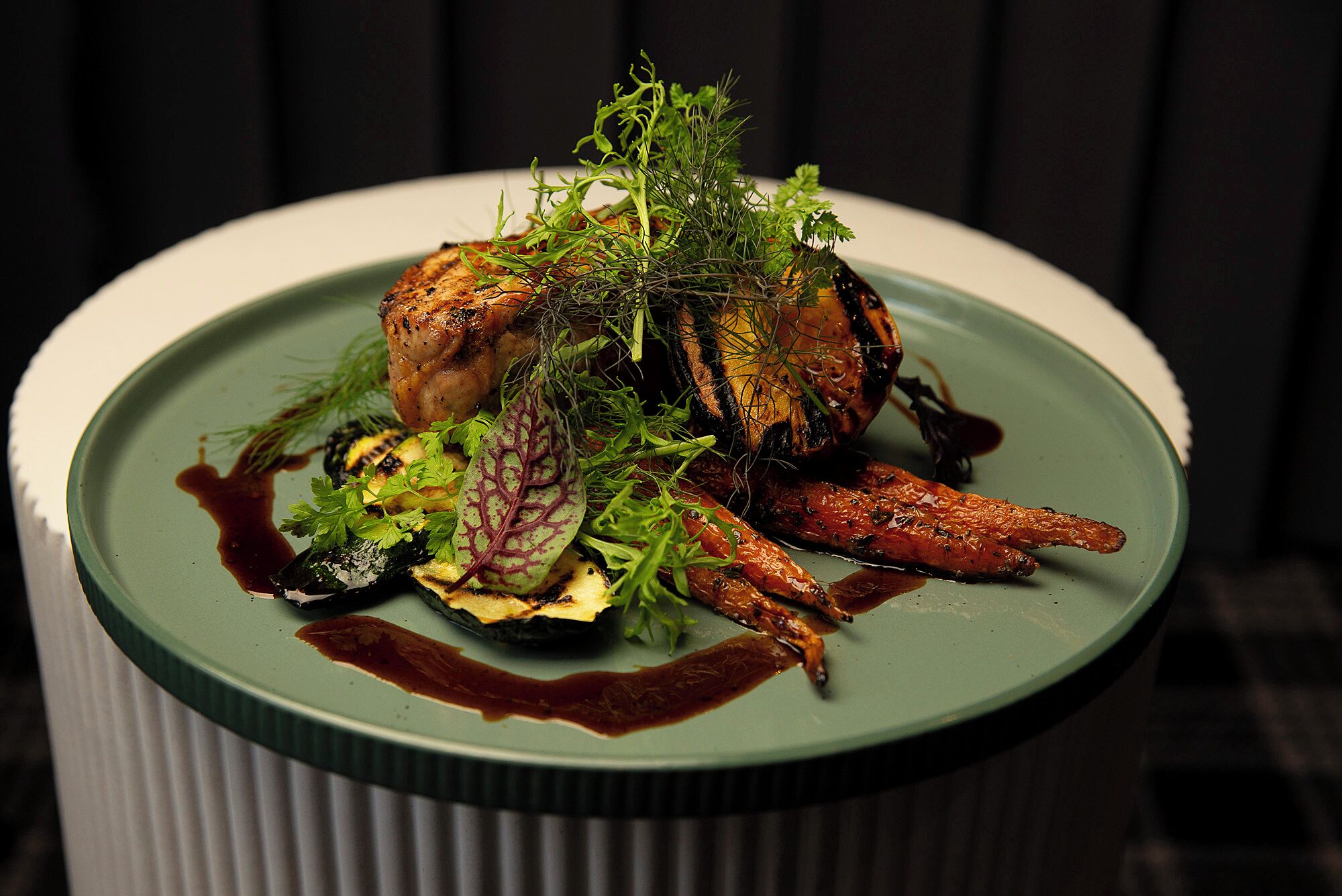 Une assiette de nourriture comprenant une variété de légumes et un morceau de viande, le tout agrémenté d’herbes aromatiques.