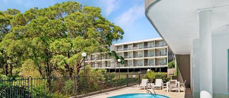A swimming pool with a view of a multi-story building and trees.