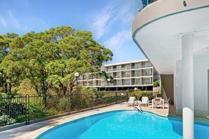 Una piscina con vistas a un edificio de varios pisos y árboles.