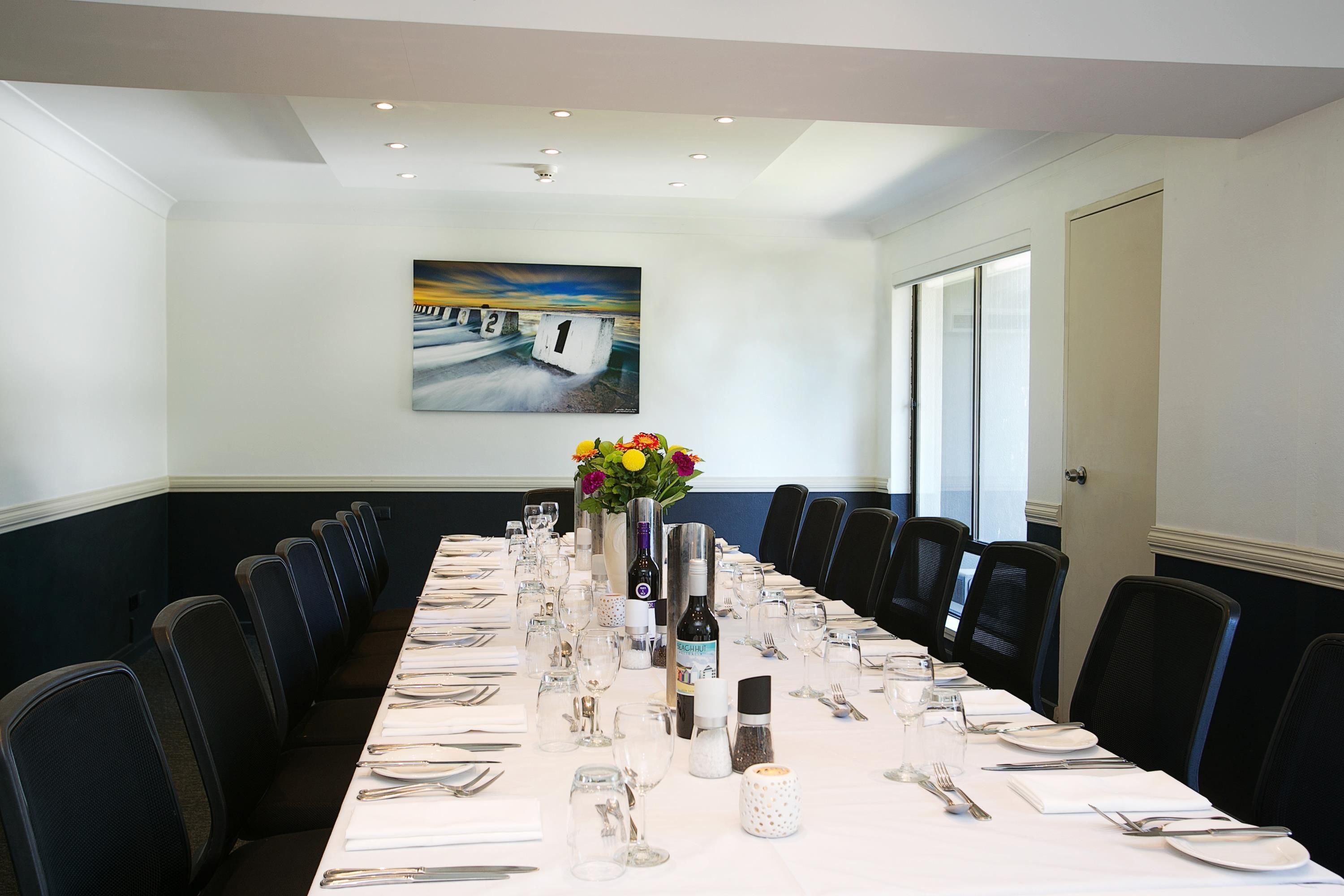 Una sala de conferencias con una larga mesa dispuesta para una reunión, sillas alrededor y un cuadro en la pared.