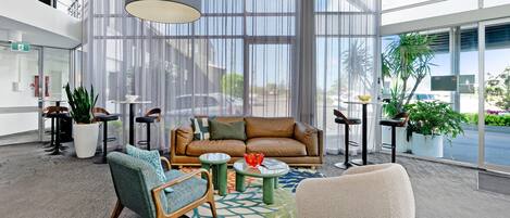 Un moderno vestíbulo con un sofá de cuero, mesas redondas y plantas en macetas.