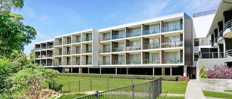 Un hôtel à plusieurs étages doté de balcons, d’une pelouse bien entretenue et offrant une vue sur un ciel dégagé.