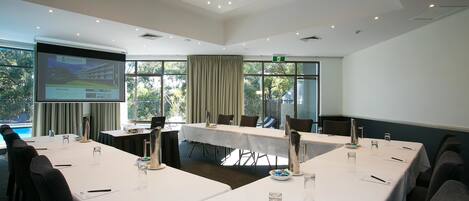 A conference room with a long table, chairs, a projector screen, and a view of the outdoors.
