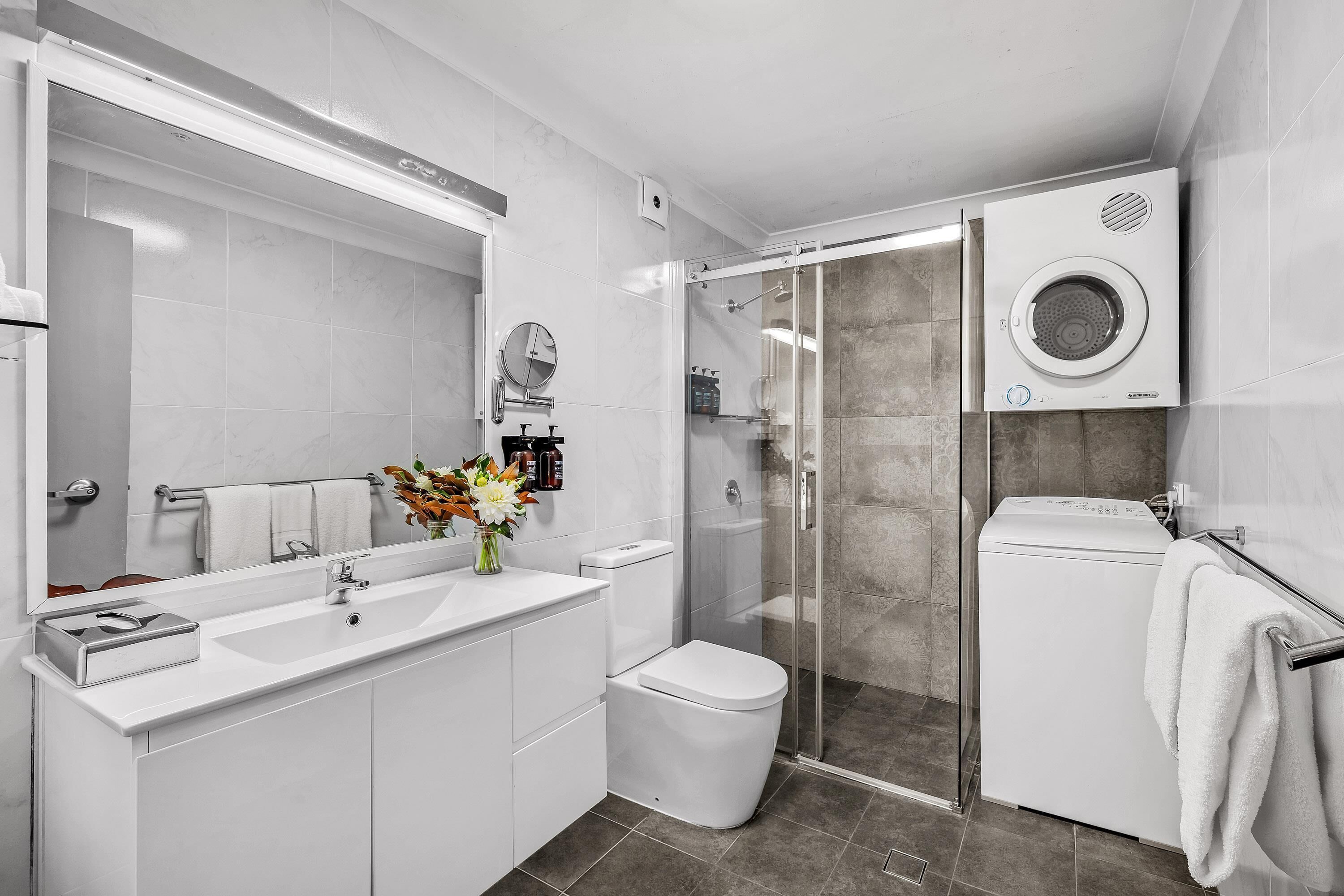 Een moderne badkamer met een glazen douchecabine, een ingebouwde wasmachine en een grote spiegel boven de wastafel.