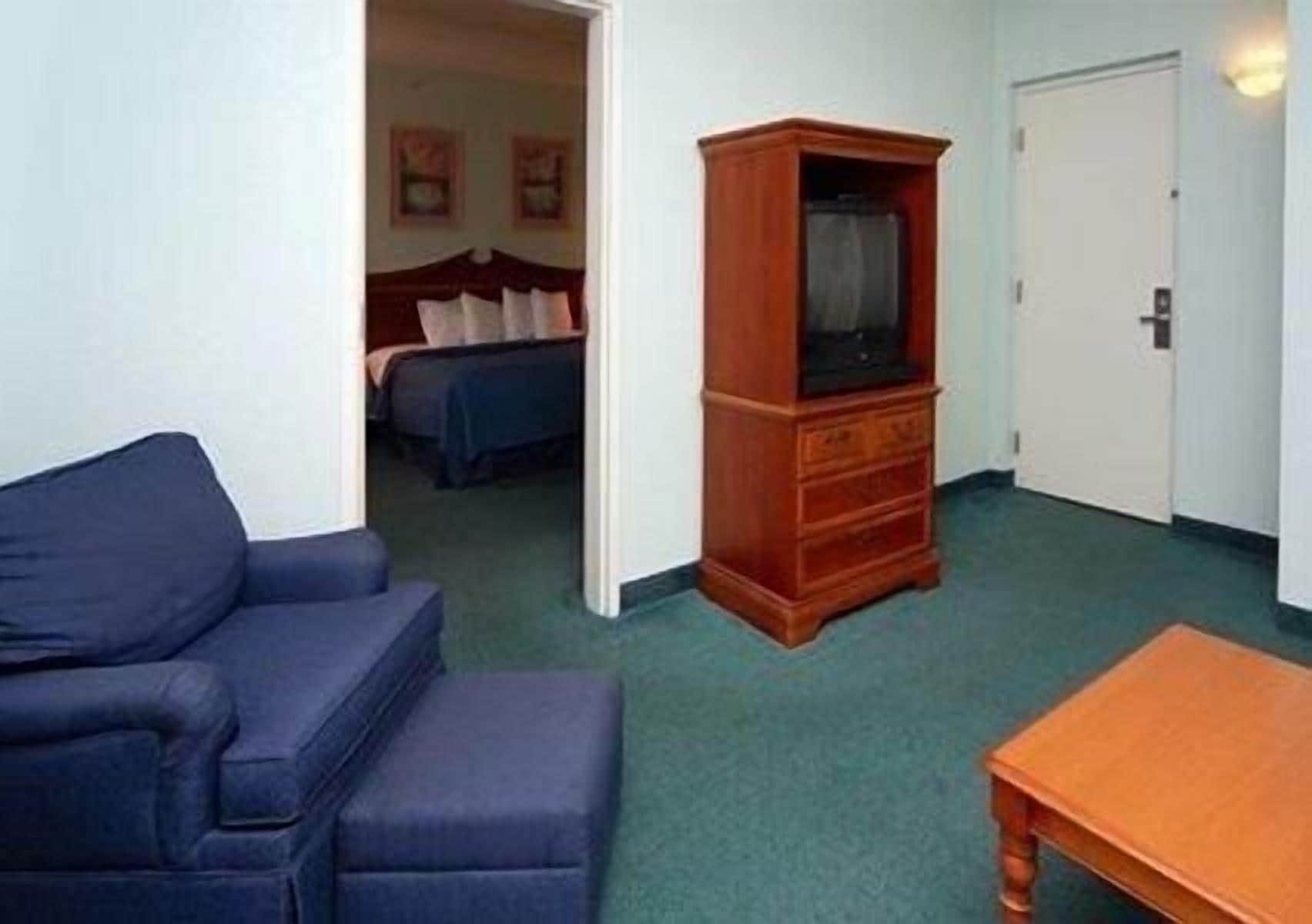 Una habitación de hotel compacta con un sofá azul, un aparador de madera y una cama con colcha azul.