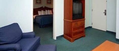 Une chambre d’hôtel de taille modeste, avec un canapé bleu, une armoire en bois et un lit recouvert d’une couverture bleue.