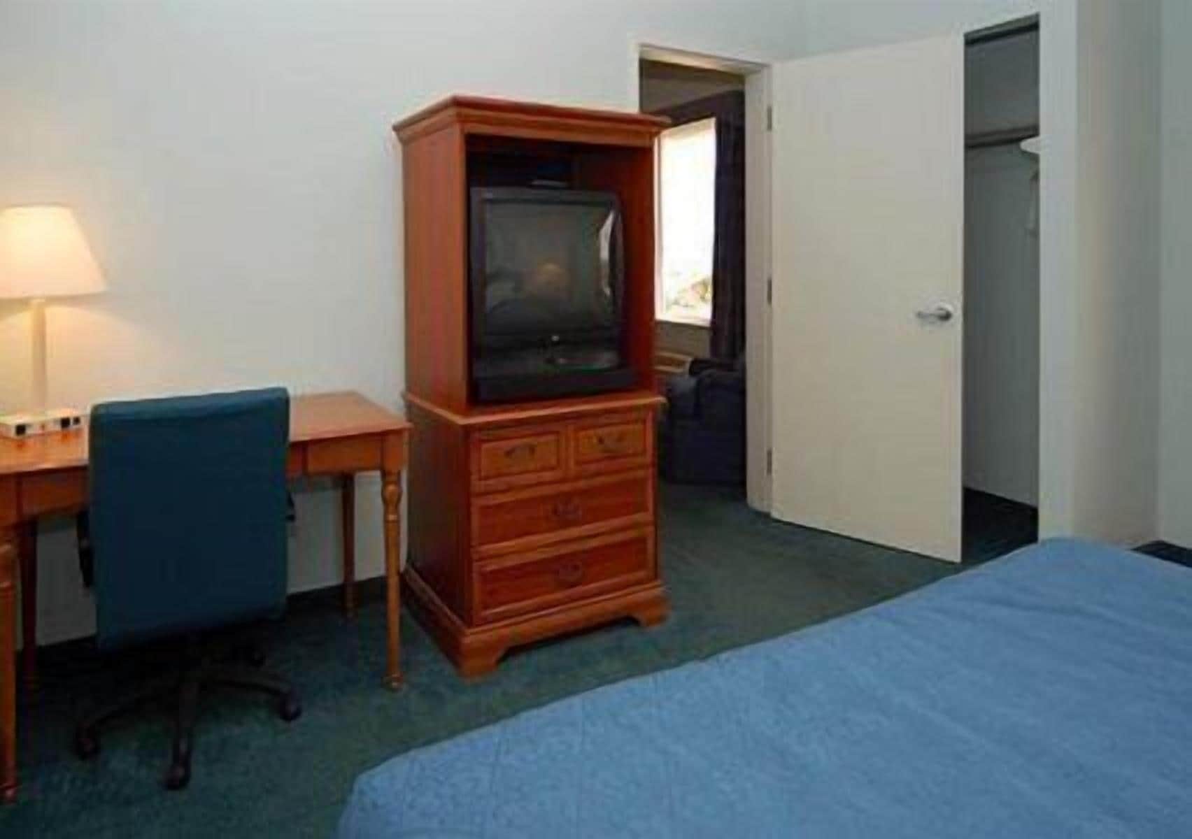Een hotelkamer met een houten dressoir, een bureau met een lamp, een blauwe stoel en een bed.