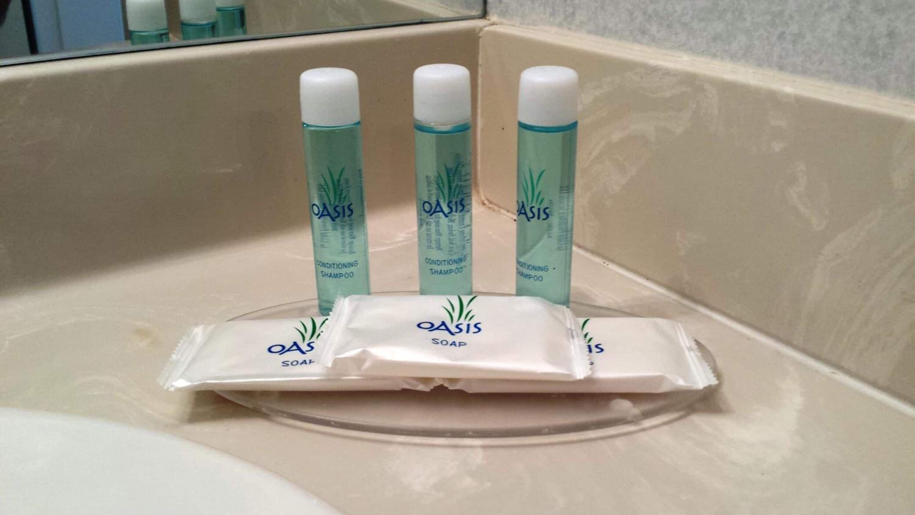 Three Oasis shampoo bottles and a bar of Oasis soap in a bathroom sink.