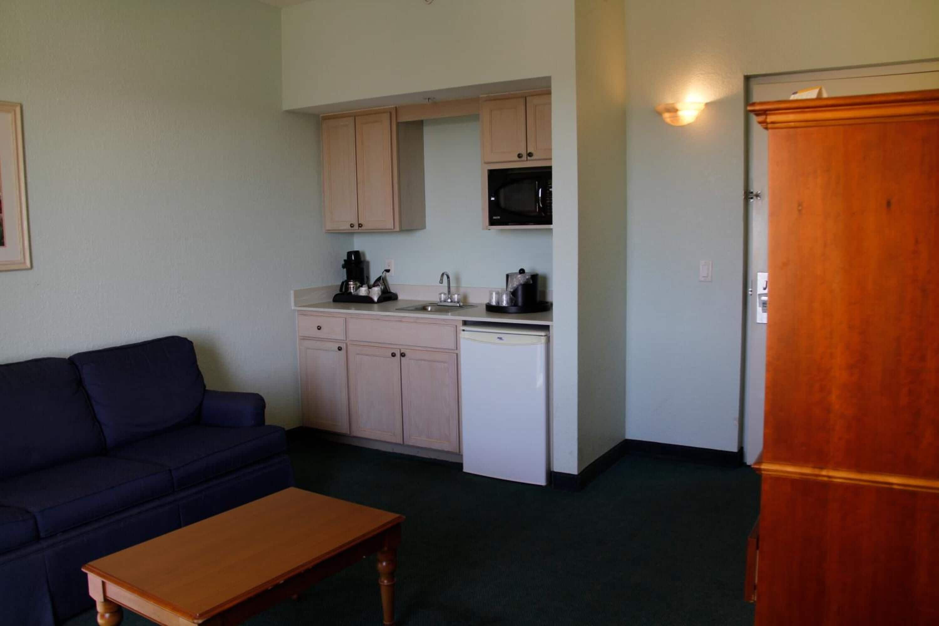 Un espacio habitable compacto con kitchenette, un sofá y una mesa de madera.